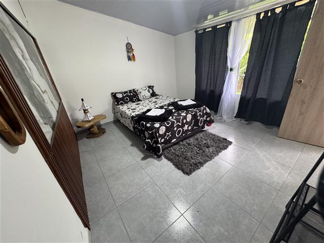 eco-hotel-gaia-11 - Turismo en el Eje Cafetero, Alquiler de Fincas en el Quindio Small bedroom with a double bed in black-and-white bedding, a gray rug, and a window with dark curtains.