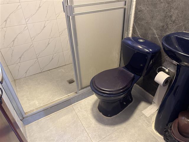 eco-hotel-gaia-12 - Turismo en el Eje Cafetero, Alquiler de Fincas en el Quindio Black toilet beside a frosted glass sliding shower door and a dark blue pedestal sink in a compact bathroom.