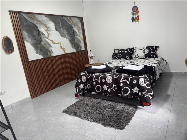eco-hotel-gaia-13 - Turismo en el Eje Cafetero, Alquiler de Fincas en el Quindio Double bed in a bright bedroom with a black-and-white starry quilt, folded towels on top, a gray shag rug, a wooden panel wall, a dreamcatcher, and a small nightstand.