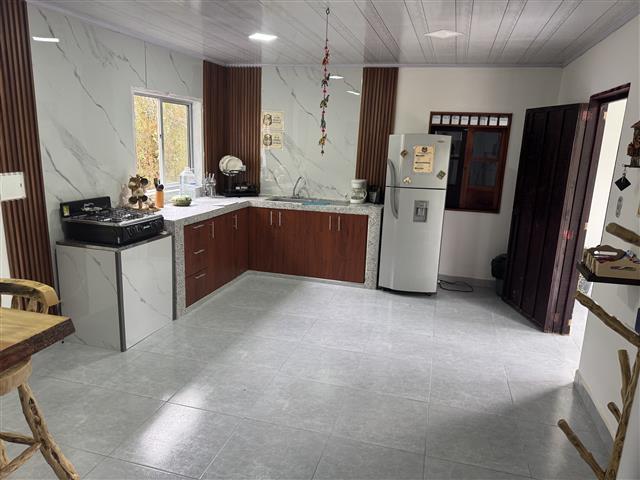 eco-hotel-gaia-14 - Turismo en el Eje Cafetero, Alquiler de Fincas en el Quindio L-shaped kitchen with brown cabinets, grey countertops, stove, fridge, and a window; tiled floor.