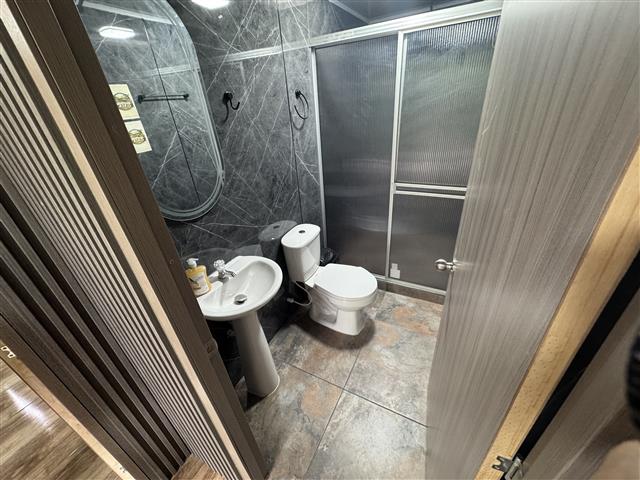 eco-hotel-gaia-17 - Turismo en el Eje Cafetero, Alquiler de Fincas en el Quindio Small bathroom with gray marble tiles, pedestal sink, toilet, and a frosted glass sliding shower door; door is open to the room.