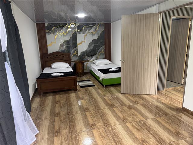 eco-hotel-gaia-20 - Turismo en el Eje Cafetero, Alquiler de Fincas en el Quindio Twin-bedroom hotel with two beds, folded towels on each, a wooden floor, marble wall art, and an open doorway to the hallway.