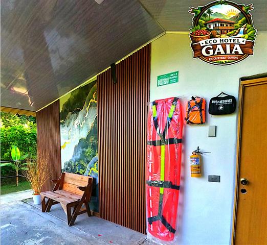 eco-hotel-gaia-6 - Turismo en el Eje Cafetero, Alquiler de Fincas en el Quindio Eco Hotel Gaia logo on the wall near a doorway; an orange life jacket hangs beside the door with a fire extinguisher nearby, and a wooden bench outside.
