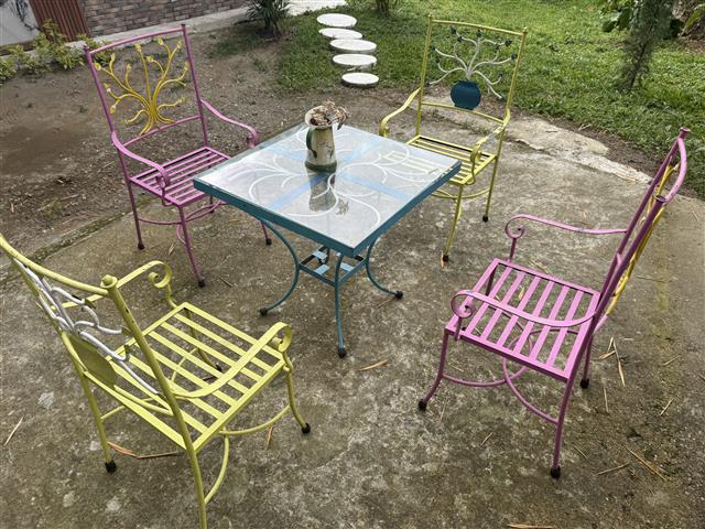 eco-hotel-gaia-8 - Turismo en el Eje Cafetero, Alquiler de Fincas en el Quindio Colorful metal patio set with six pastel chairs around a glass-topped table, a small potted plant in the center.